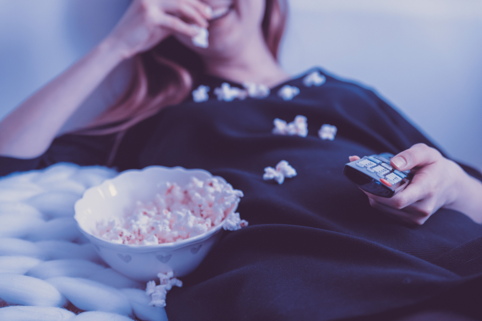 A woman on a sofa eating popcorn and holding a TV remote