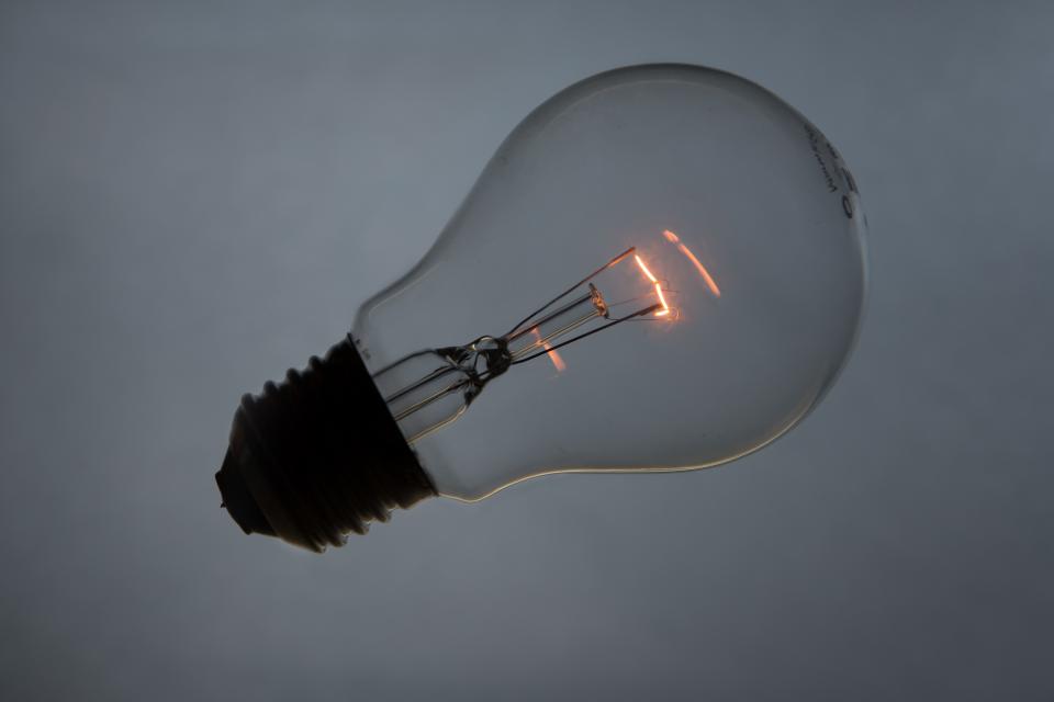 A clear light bulb with a glowing filament against a gray background