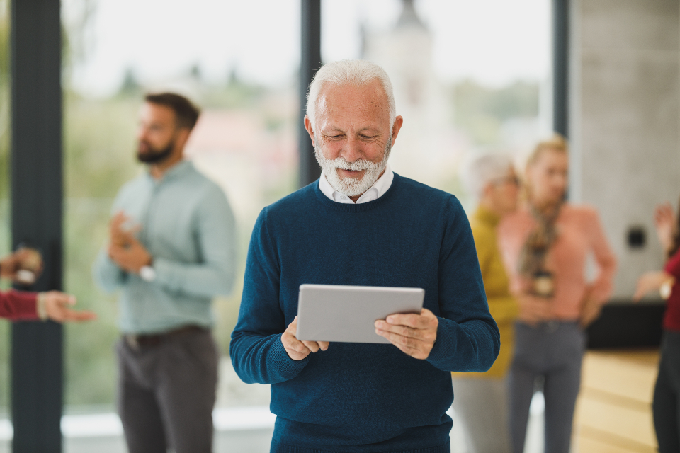 An older man in a blue sweater looking at a tablet
