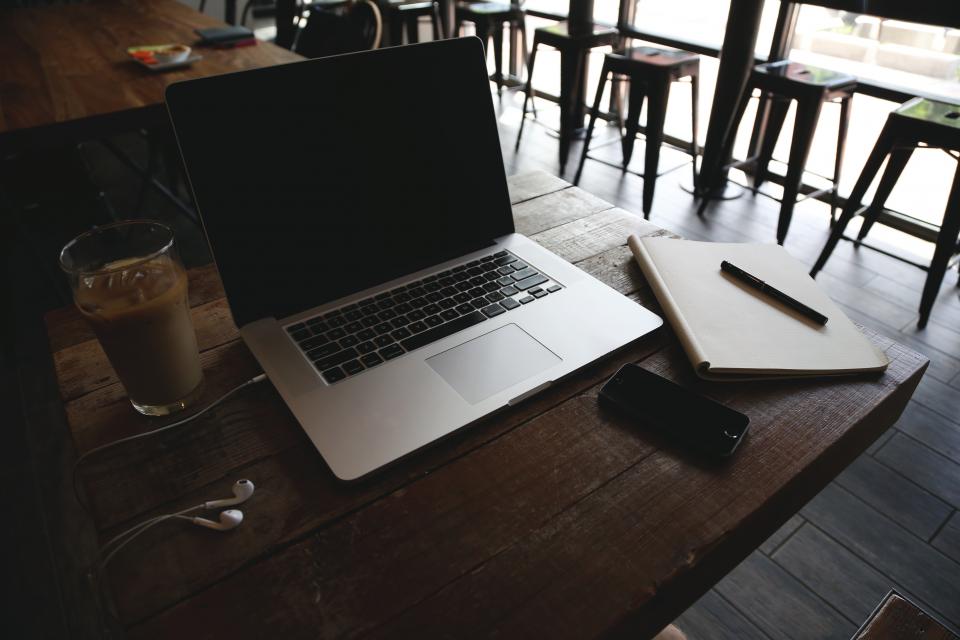 A laptop, a notebook and a phone on a wooden table in an empty cafe